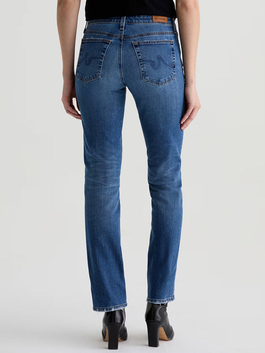 Person wearing AG Jeans Sandra AG-ed™ Low-Rise Straight in 15 Years Prague and black heeled boots, shown from the back against a plain background.