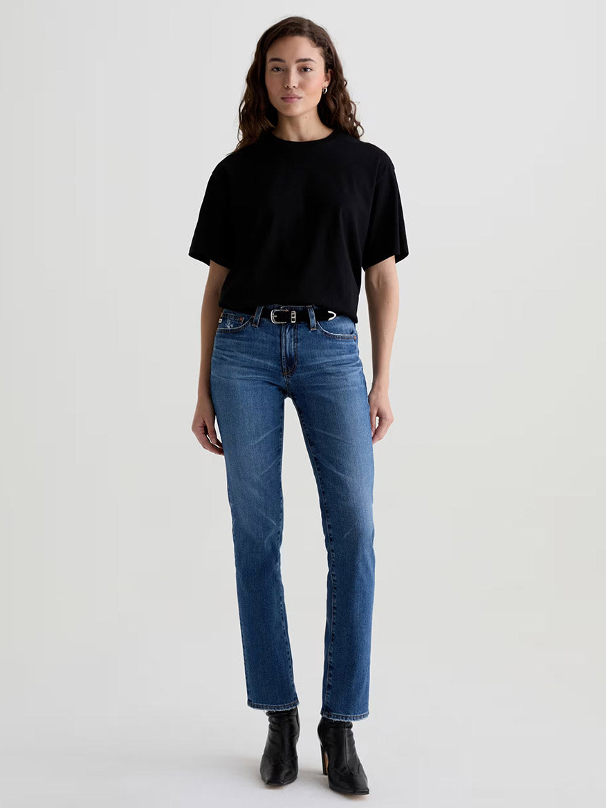 Woman standing against a plain background, wearing a black t-shirt, black belt, black ankle boots, and AG Jeans Sandra AG-ed™ Low-Rise Straight in 15 Years Prague.