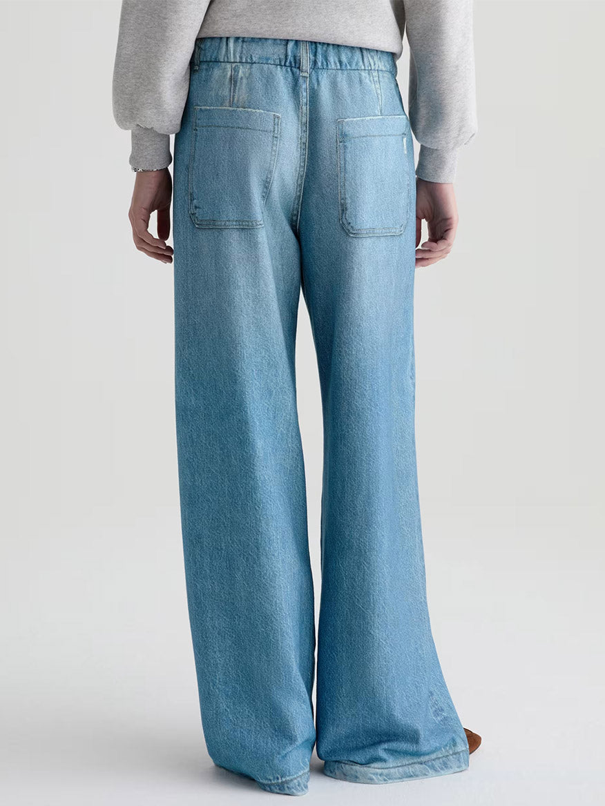 Model shown from the back wears AG Jeans Stella Off-Duty Denim Sweatpant in Splash and a grey French terry sweatshirt against a neutral background.
