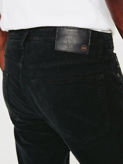 A person wearing AG Jeans Tellis Corduroy Slim Fit in Sulfur Gunpowder.