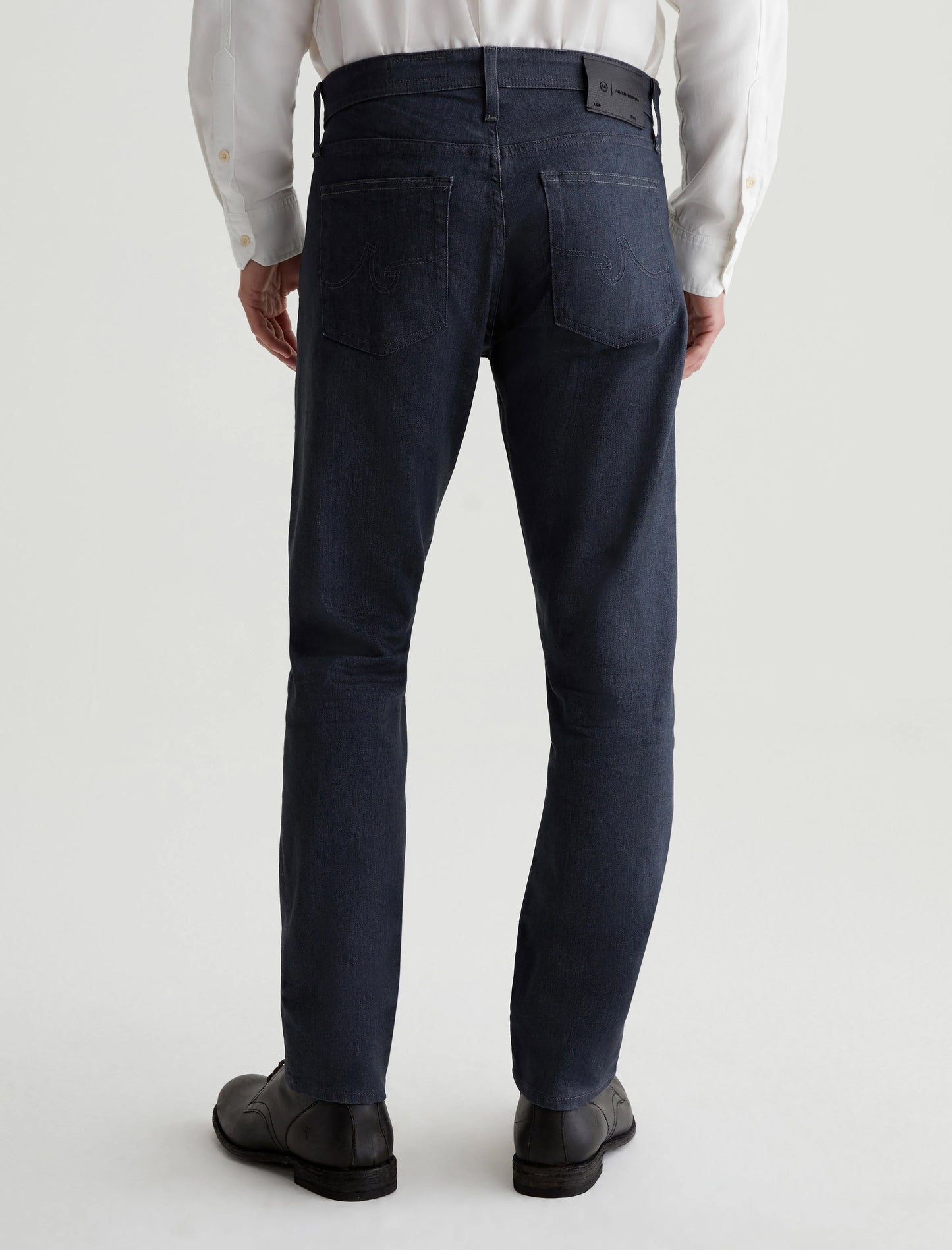 A person wearing the AG Jeans Tellis in 1 Year Reel, featuring a white shirt and slim-fit design crafted from Ashen Stretch Denim, is seen from the back.