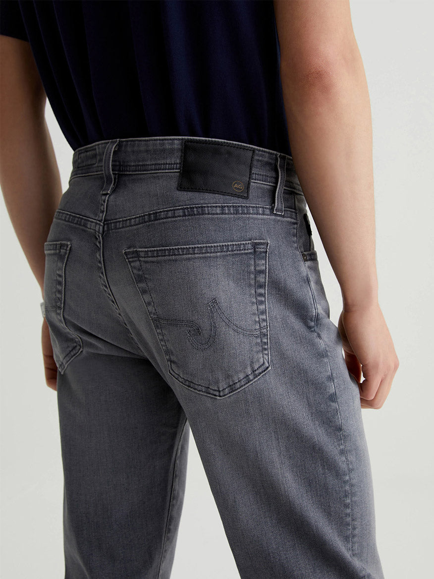 Seen from behind, a person is wearing the AG Jeans Tellis in Prestige, slim fit jeans crafted from stylish Ashen Stretch Denim featuring a distinct back pocket design.