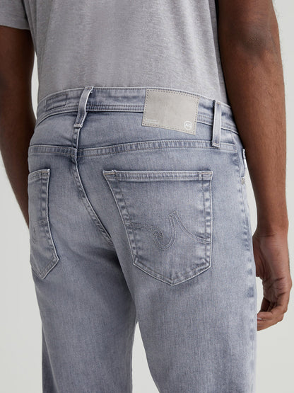 Close-up view of a man wearing AG Jeans Tellis in Vapor Wash Atwater, focusing on the back pocket and waistband with a visible leather logo patch.