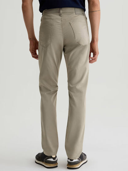 A person is seen from behind wearing AG Jeans Tellis Airluxe™ Modern Slim Pant in Dry Dust, paired with a dark shirt and black sneakers with white soles.