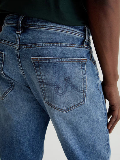 Close-up of a person wearing AG Jeans Tellis in Horsetail, featuring indigo denim and a wave-like stitched design on the back pocket.