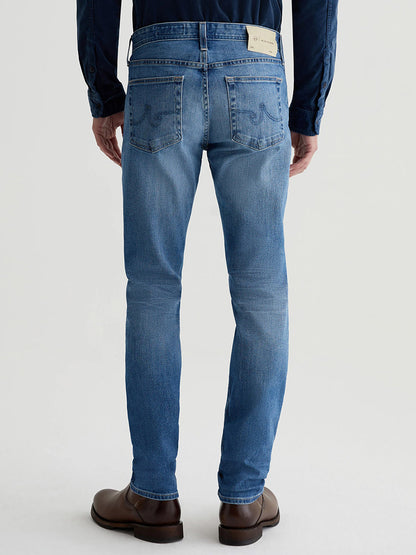 A person wearing AG Jeans Tellis in 19 Years Broad slim-fit jeans and brown shoes is shown from the back.