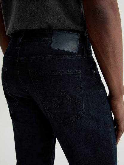 A person shown from the waist down and viewed from behind, wearing AG Jeans Tellis in Tamarack with a dark shirt.