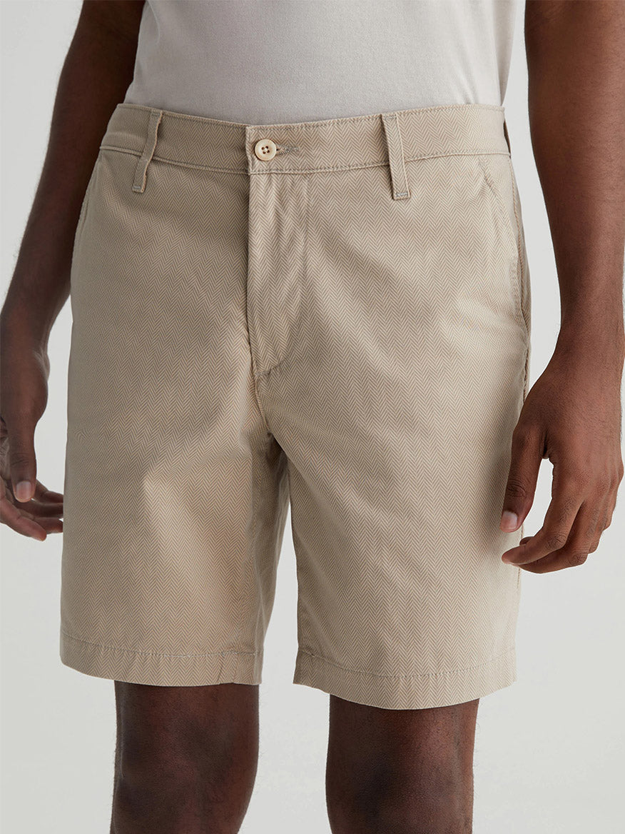 A person wearing AG Jeans Wanderer Short in Parquet Khaki Multi and a light-colored shirt is standing with their arms relaxed at their sides. The photo focuses on the shorts from waist to mid-thigh.