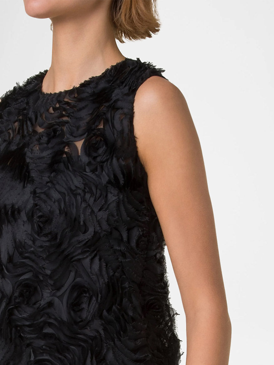 A person wears the Akris Punto Sleeveless 3D Carnation Knee Length Dress in black, facing forward, showcasing the elegant shift silhouette adorned with an embroidered floral design. Only their upper body is shown.