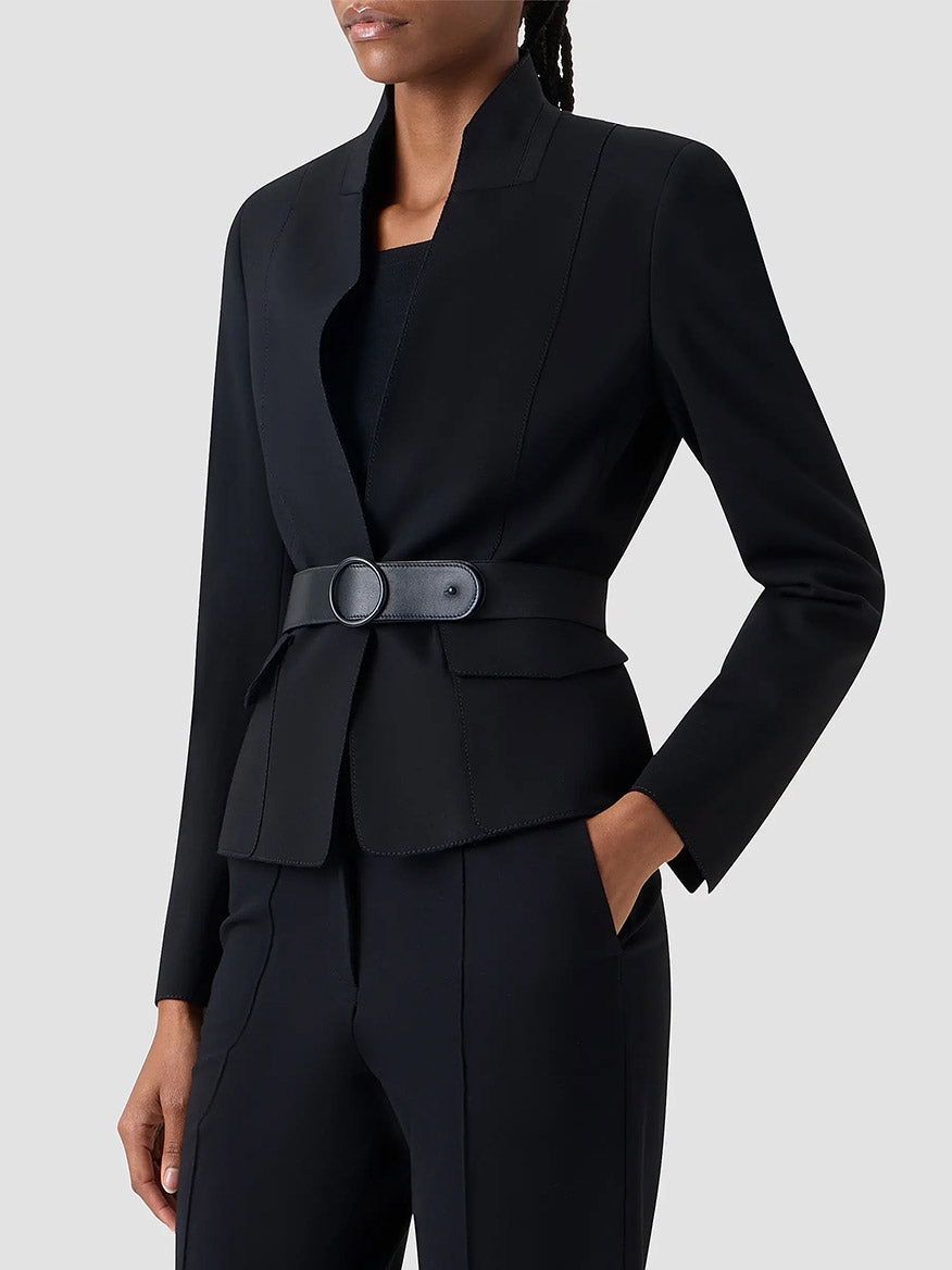 A person wears the Akris Punto Belted Jacket in Black with matching pants, one hand in a pocket, standing against a plain light background.