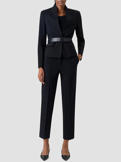 A person wearing the Akris Punto Belted Jacket in Black, paired with a black top, straight-leg trousers, and black heels, stands against a plain light grey background.