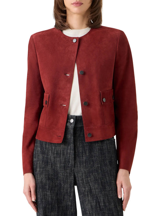 A person wears the Akris Punto Boxy Suede Jacket in Pomegranate, featuring utility-inspired pockets and a jewel neckline, layered over a white top and dark textured pants; photographed from the waist up.