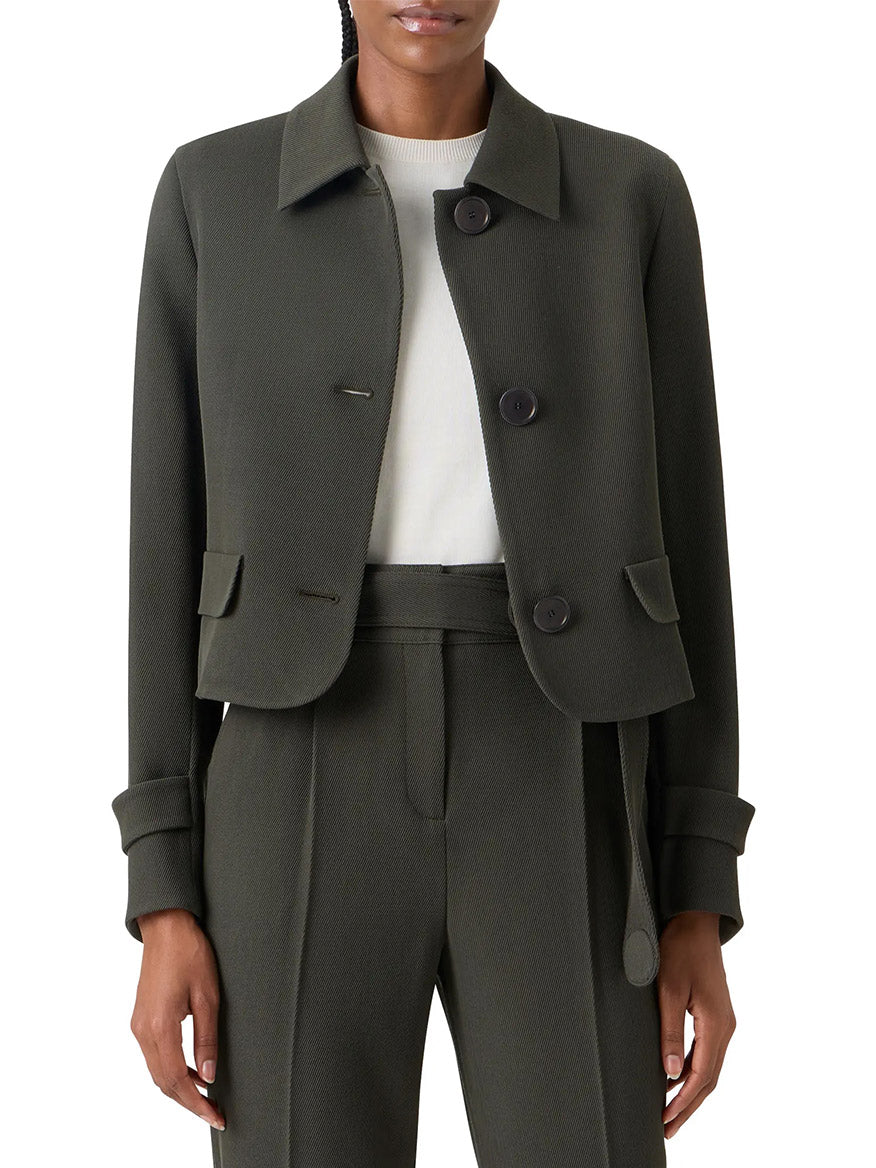 A person wears the Akris Punto Boxy Wool Tricotine Jacket in Olive, featuring decorative pocket flaps and large buttons, paired with matching high-waisted trousers and a white top.
