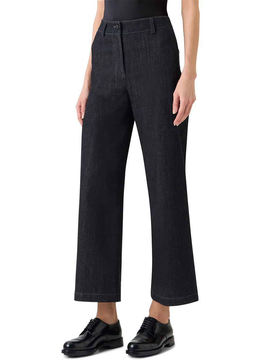 Person wears the Akris Punto Caia High-Rise Straight Leg Black Denim jeans, paired with a black top and black dress shoes, standing against a plain white background.