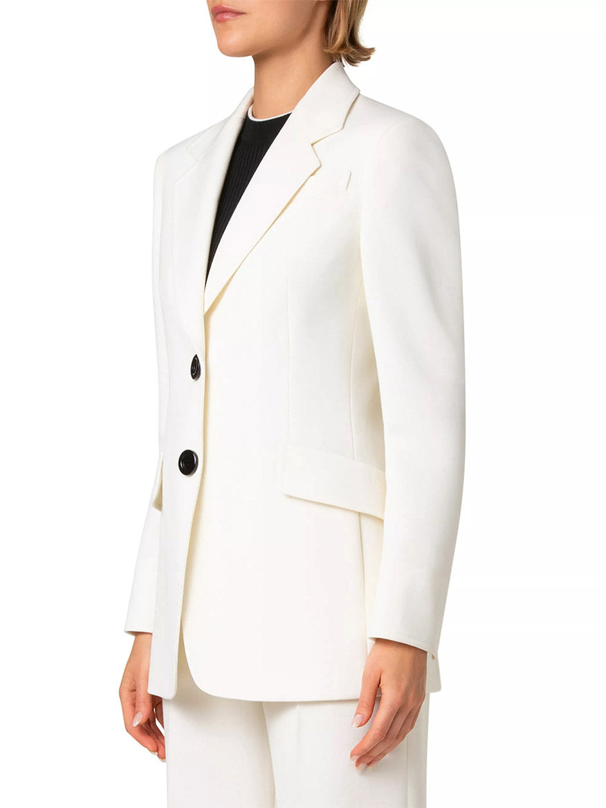 A person stands against a plain backdrop, wearing the Akris Punto Captain Gabardine Wool Blazer in cream with striking contrast buttons over a sleek black shirt.