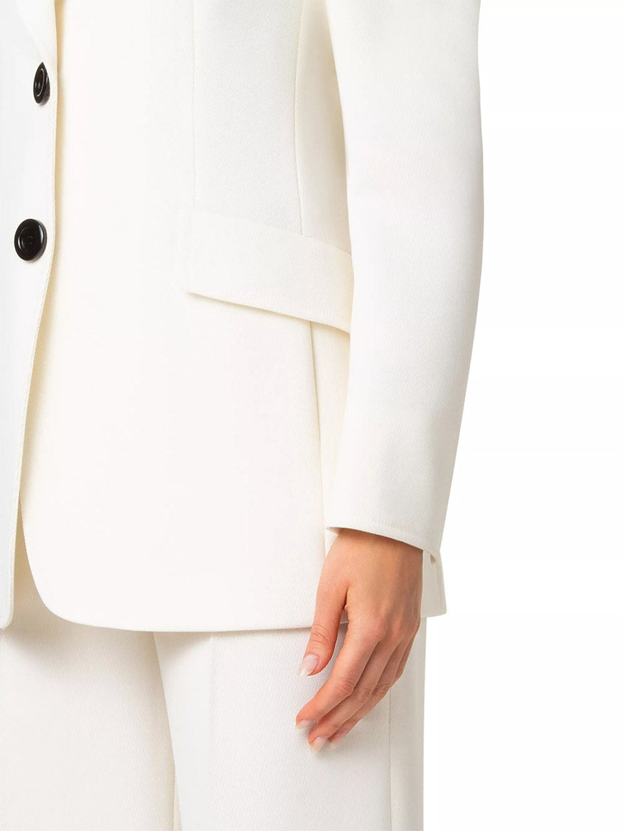 A close-up of a person wearing the Akris Punto Captain Gabardine Wool Blazer in Cream highlights their right arm and hand at rest, elegantly showcasing the cream gabardine fabric with sophisticated contrast buttons.