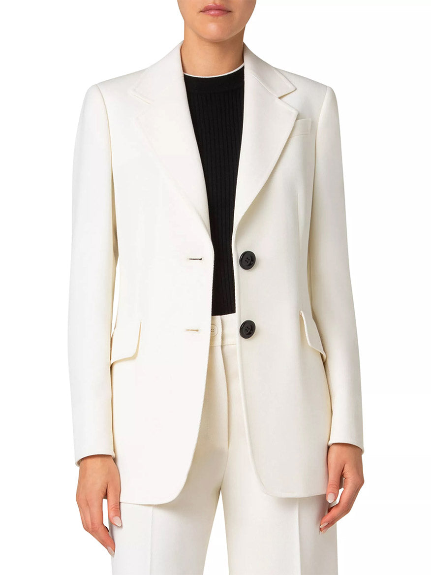 A person wears the Akris Punto Captain Gabardine Wool Blazer in Cream over a black top, pairing it with matching white trousers for a sleek and polished look.