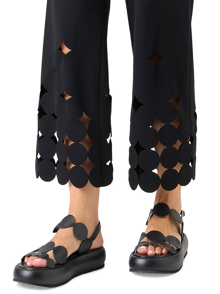 Wearing Akris Punto Chieko Dropping Dot Cut Out Ankle Pant in Black with black sandals, the visible lower legs showcase the straight-leg silhouette and bold geometric cutout details at the hem.