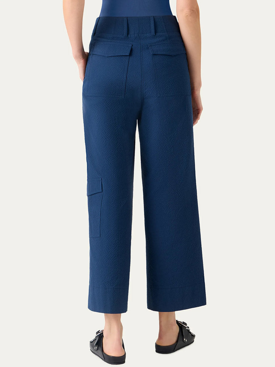 Person wearing Akris Punto Cliff Seersucker Cargo Pants in dark blue, featuring a high-waisted, wide-leg cargo style with back and side pockets, viewed from behind.