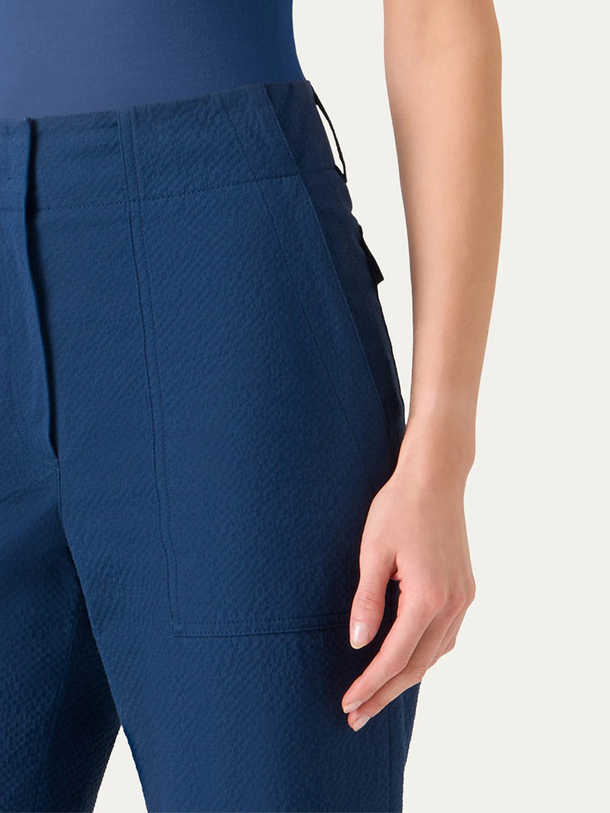A person wearing Akris Punto Cliff Seersucker Cargo Pants in dark blue; the lower torso and right arm are visible, highlighting the high-waisted, textured design with large front pockets.