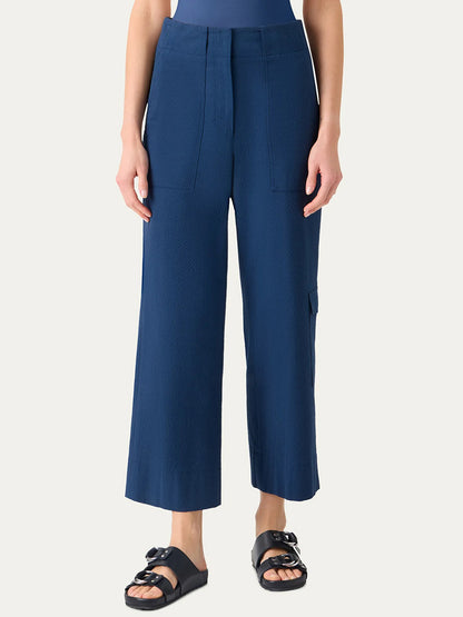 Person wears Akris Punto Cliff Seersucker Cargo Pants in Dark Blue, featuring a high-waisted, wide-leg cargo style with front pockets, paired with a tucked-in top and black slip-on sandals against a plain background.