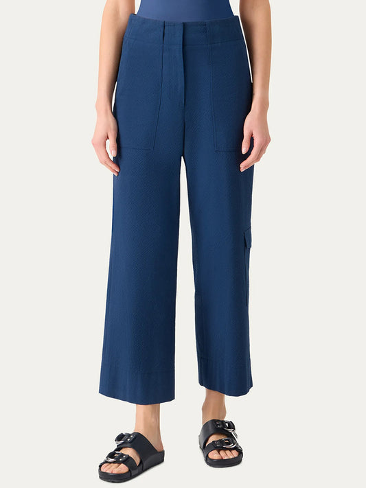 Person wears Akris Punto Cliff Seersucker Cargo Pants in Dark Blue, featuring a high-waisted, wide-leg cargo style with front pockets, paired with a tucked-in top and black slip-on sandals against a plain background.