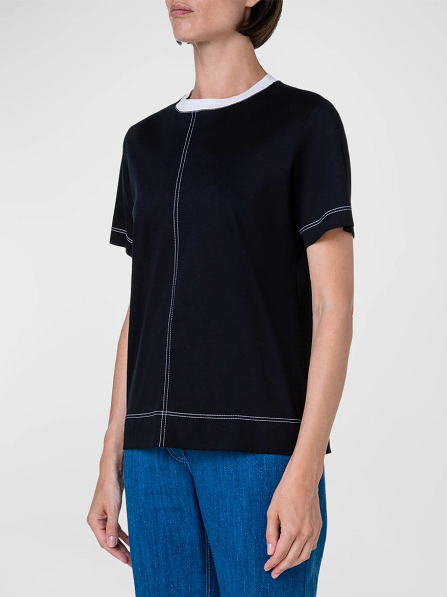 A woman wearing an Akris Punto Contrast Stitching Trim T-Shirt in Black, paired with jeans.
