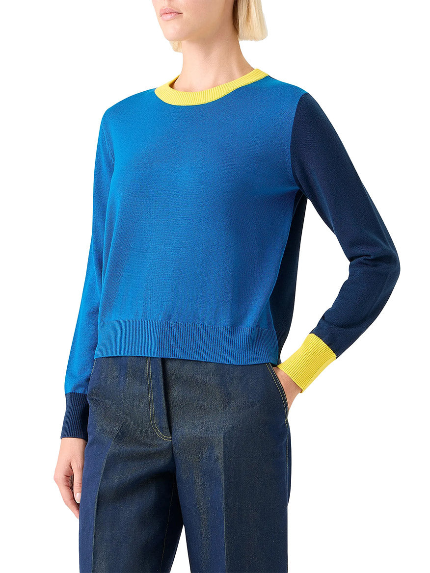 A person wearing the Akris Punto Cool Wool Colorblock Crewneck Sweater in Cobalt Blue Multi and dark blue jeans, with one arm at their side and the other hand on their hip.