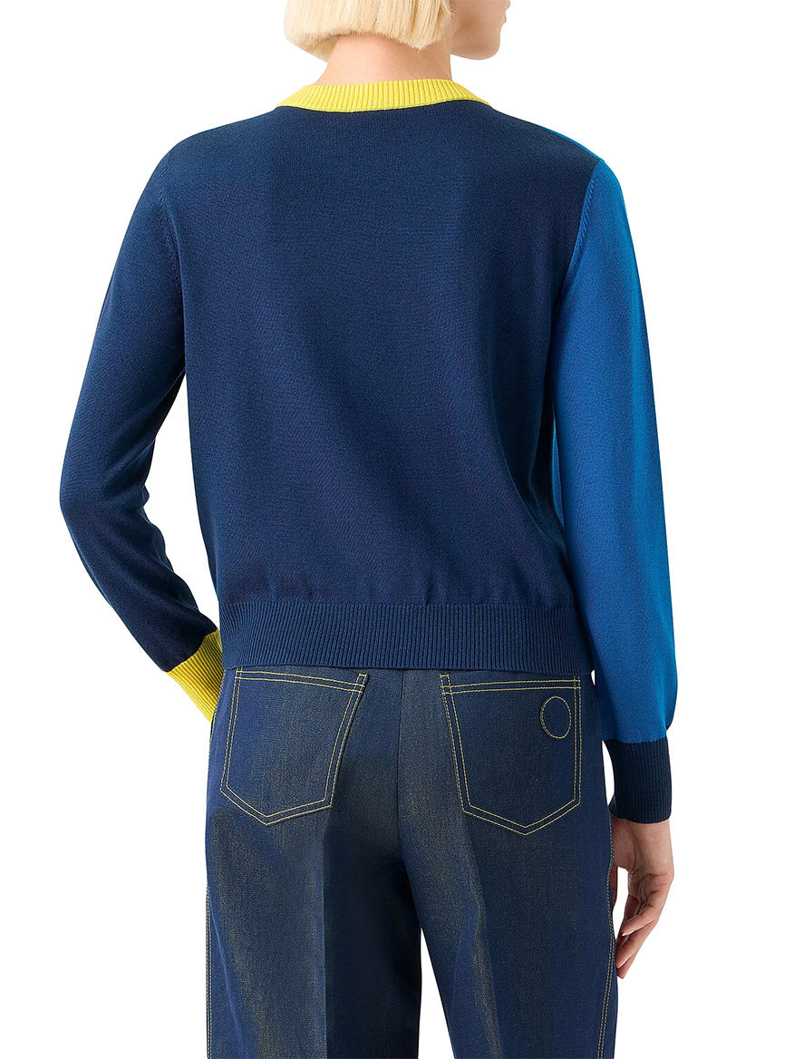 A person is shown from the back wearing the Akris Punto Cool Wool Colorblock Crewneck Sweater in Cobalt Blue Multi, featuring a yellow collar and cuffs, paired with dark jeans accented by yellow stitching.