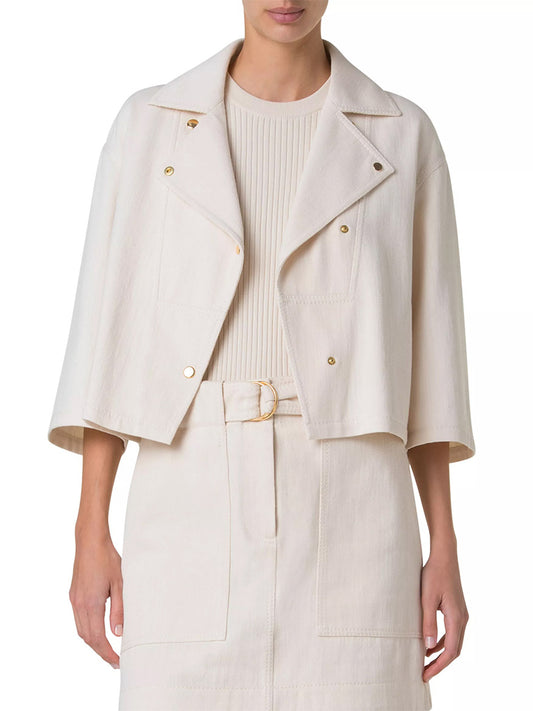 A person is wearing an Akris Punto Asymmetrical Cotton Blend Biker Jacket in Cashew, styled with button details and an asymmetric snap closure, paired with a knee-length skirt and belt.