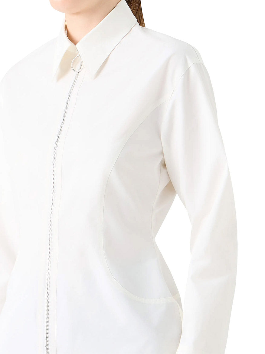 A person wears the Akris Punto Poplin Cotton Cinched Waist Shirt in Cream, featuring long sleeves, a collared neckline, front zipper with a circular pull, and signature brand detailing.