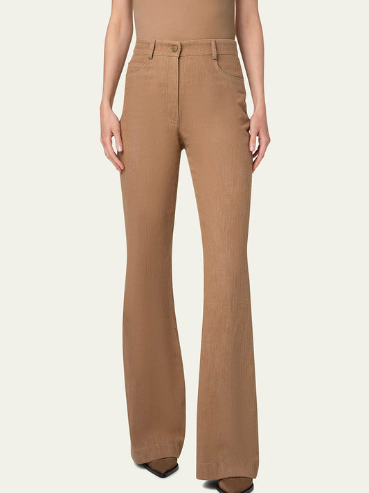 The person is wearing the Akris Punto Courtney High Rise Straight Flared Denim in Caramel with front pockets, paired with a matching brown top. The pants feature a front button and zipper closure. The shoes, partially visible under the pants, are black.