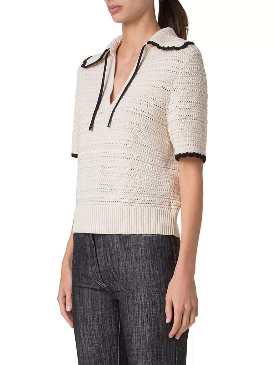 Wearing the Akris Punto Crochet Boxy Polo in Cashew/Black, featuring a cream crochet-knit short sleeve design with a scallop trim, collar, and drawstrings, pairs elegantly with dark pants.