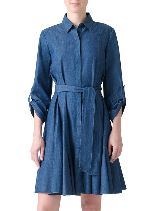 A woman wears the Akris Punto Tie-Waist Denim Shirtdress in Medium Blue, featuring an A-line silhouette, knee-length hem, long sleeves, belted waist, flared skirt, and a collar.