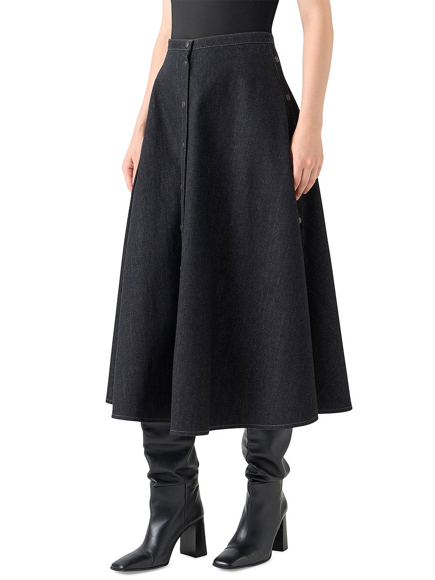 Wearing the Akris Punto Stretch Denim Snap Button Midi Skirt in Black Denim with a fitted black top, knee-high black heeled boots, and an oversized floral shirt draped over the shoulders.
