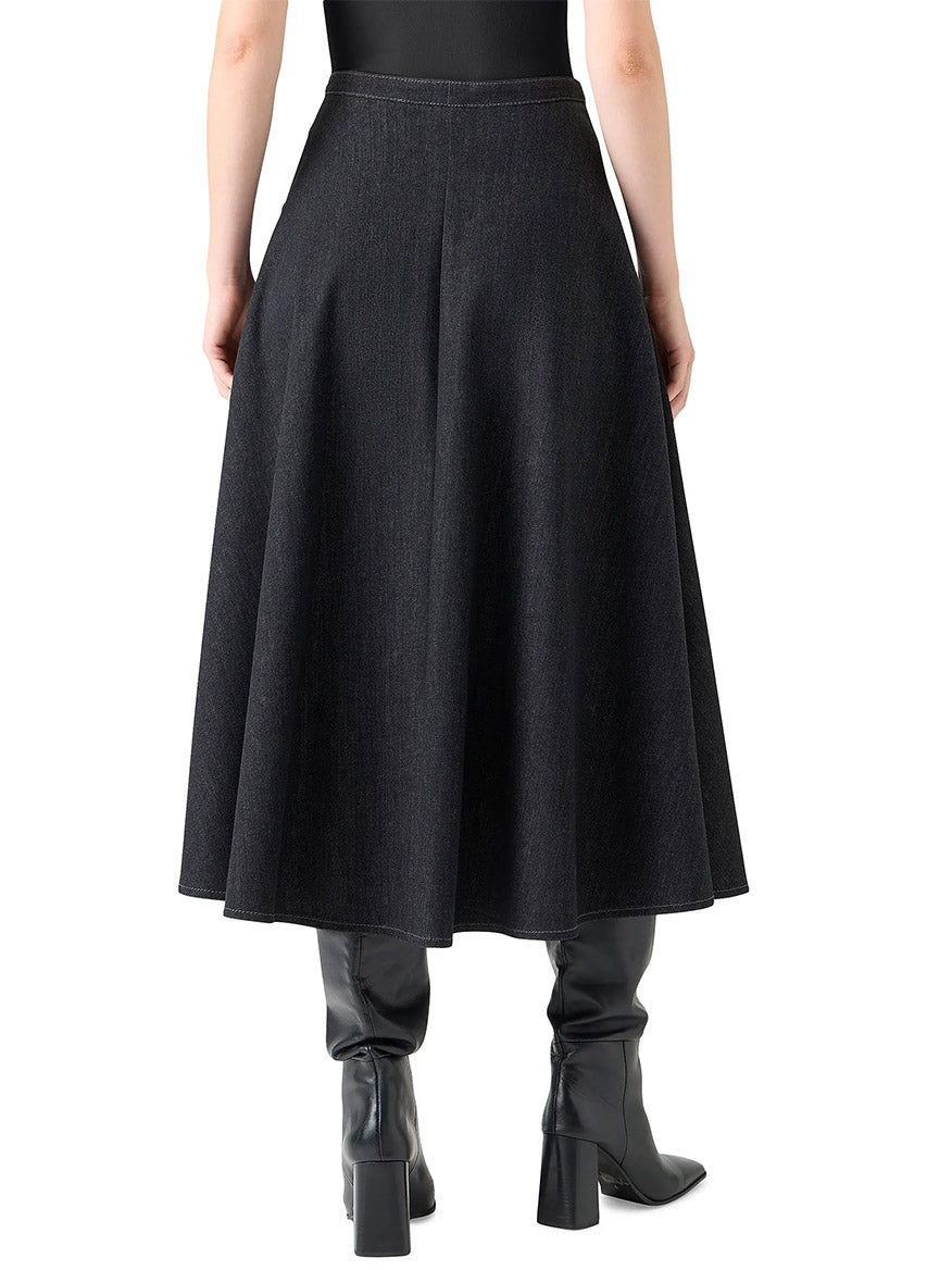 A person is seen from the back wearing an Akris Punto Stretch Denim Snap Button Midi Skirt in Black Denim, paired with an oversized floral shirt and black heeled boots.