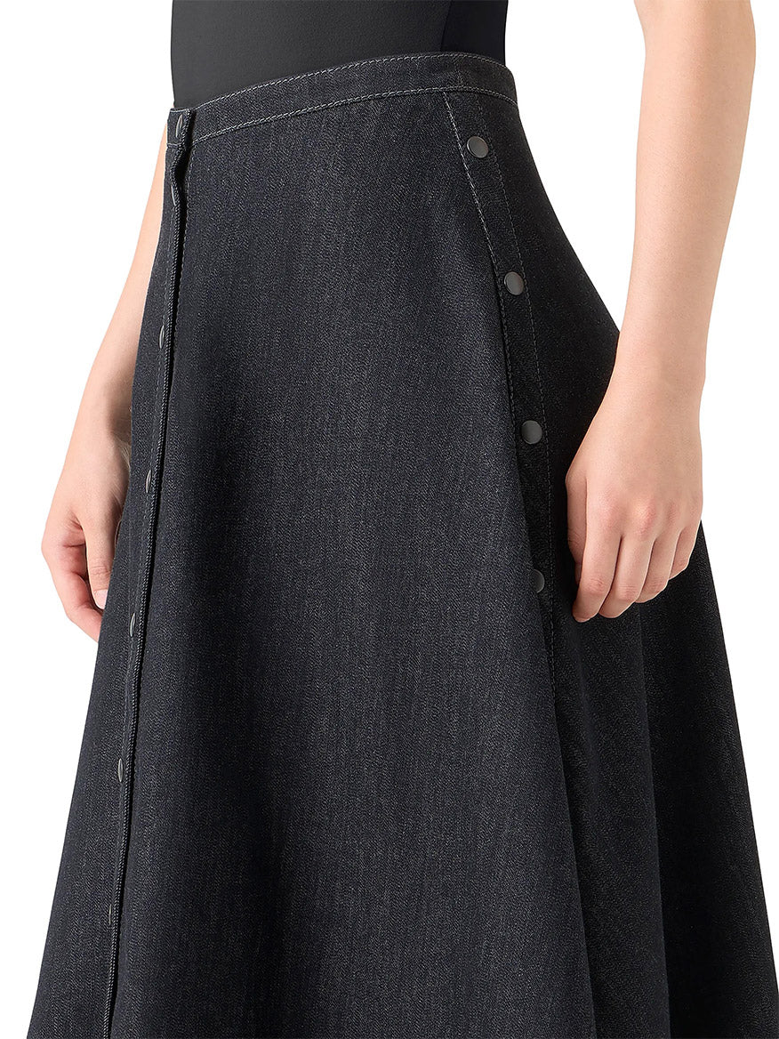 A person styles the Akris Punto Stretch Denim Snap Button Midi Skirt in black denim with a black top and an oversized floral shirt for a chic, layered outfit.