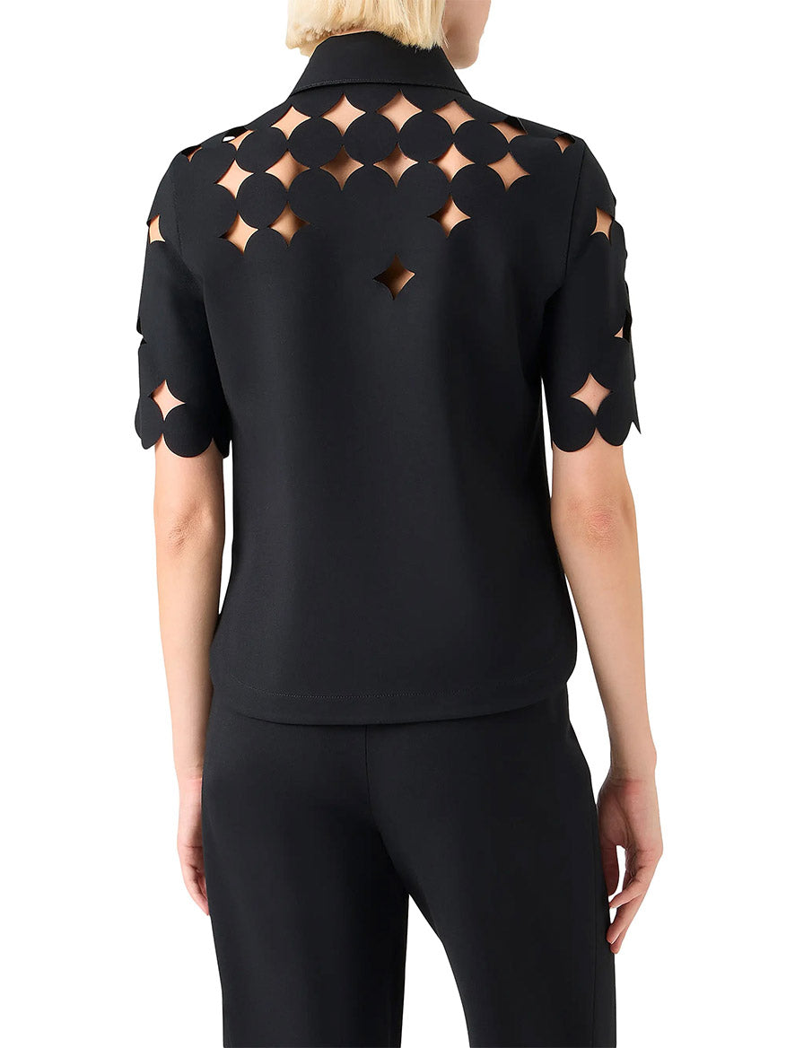 A person seen from behind wearing the Akris Punto Dropping Dot Cut Out Polo in Black, featuring geometric cut-out patterns on the back and sleeves, paired with black pants.