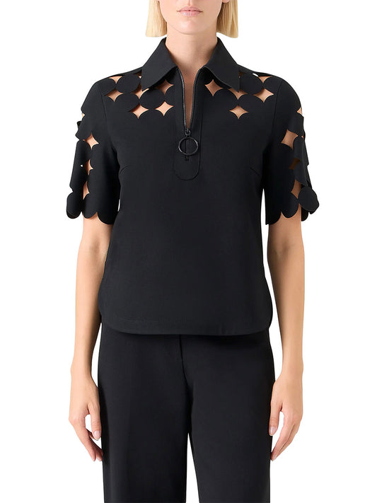 A woman wears the Akris Punto Dropping Dot Cut Out Polo in Black, featuring geometric sleeve and shoulder cut-outs, a half-zip front, and paired with matching black pants.