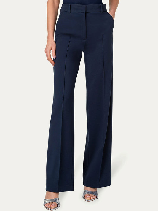 Person wearing high-waisted, navy blue Akris Punto Chiaro Jersey Straight Leg Pant in Navy with a wide-leg fit and hands in pockets, paired with silver open-toe sandals. The pants have center pleats and a structured fit.