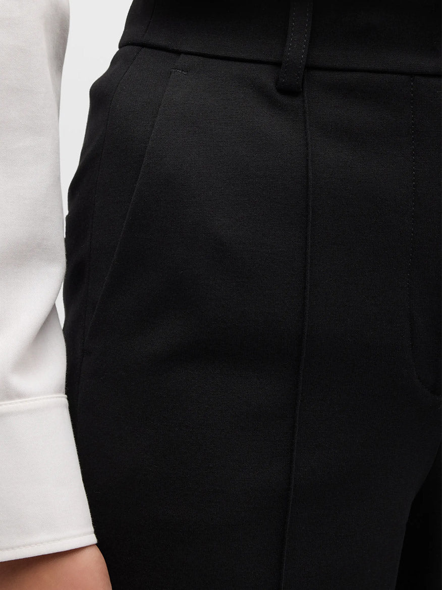 Close-up of a person wearing black Akris Punto Elements Ferry Tapered Jersey Pants in Black and a white shirt. The focus is on the waistband and pocket area of the sleek jersey pants, showcasing their tapered fit.