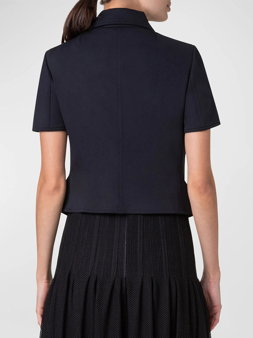 Rear view of a person wearing an Akris Punto Elbow Sleeve Neoprene Biker Jacket in Black over a pleated black skirt.