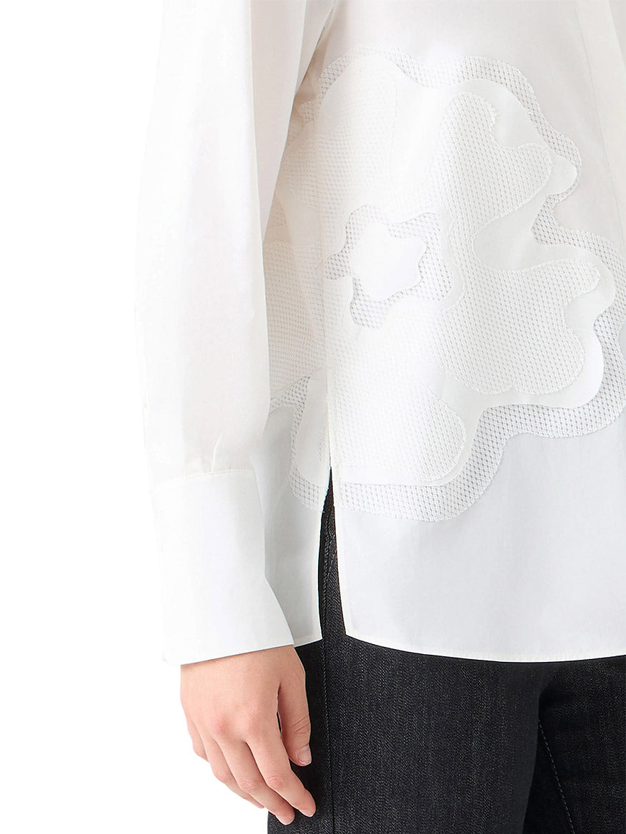 A person wearing the Akris Punto XL Pop Dot Flower Applique Button Down Blouse in Cream with black pants, shown from the side with only the left arm and torso visible.