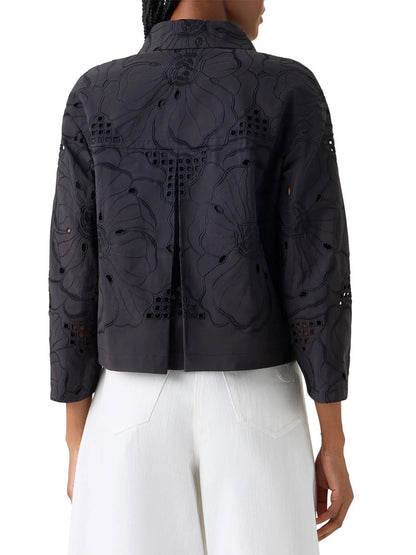 A person is seen from the back wearing the Akris Punto Flower Eyelet Embroidered Jacket in Black, featuring dark fabric with oversized floral embroidery, paired with white pants.