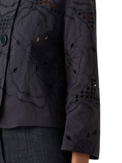 Close-up of a person wearing the Akris Punto Flower Eyelet Embroidered Jacket in Black, featuring cotton-poplin fabric, wide sleeves, oversized floral eyelets, and paired with dark jeans.