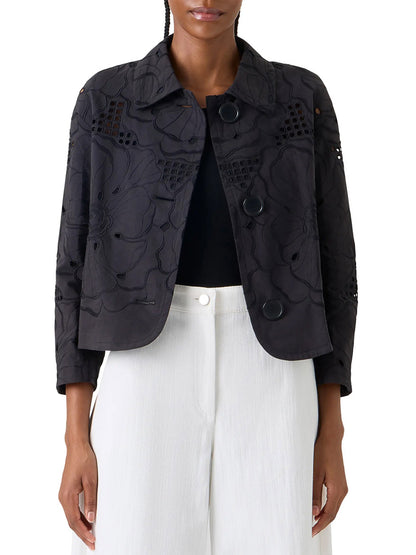 A person wearing the Akris Punto Flower Eyelet Embroidered Jacket in Black over a black top and white pants, shown from the waist up.
