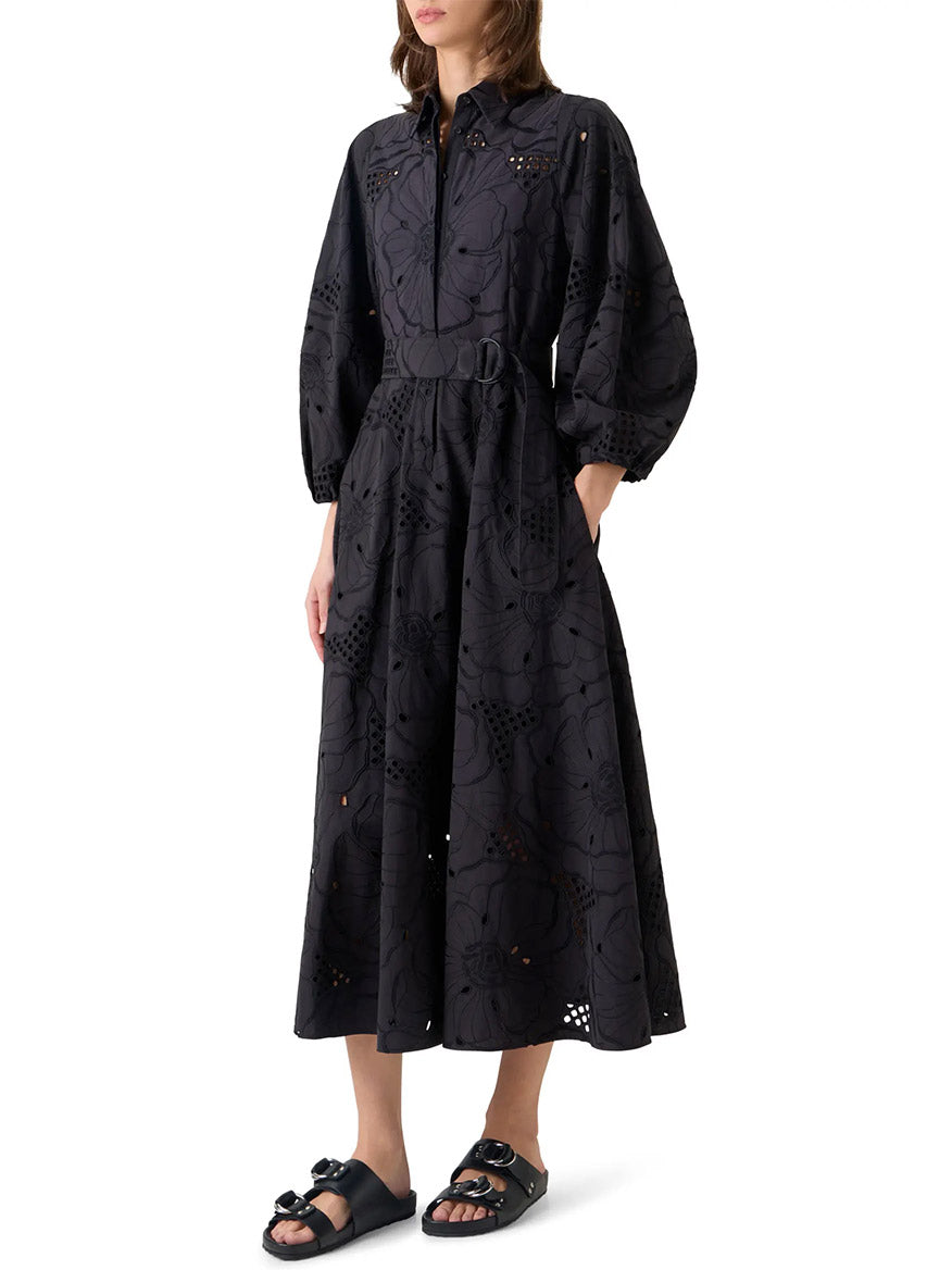 Woman wearing the Akris Punto Flower Eyelet Embroidered Midi Dress in black, paired with flat black sandals, standing against a white background.