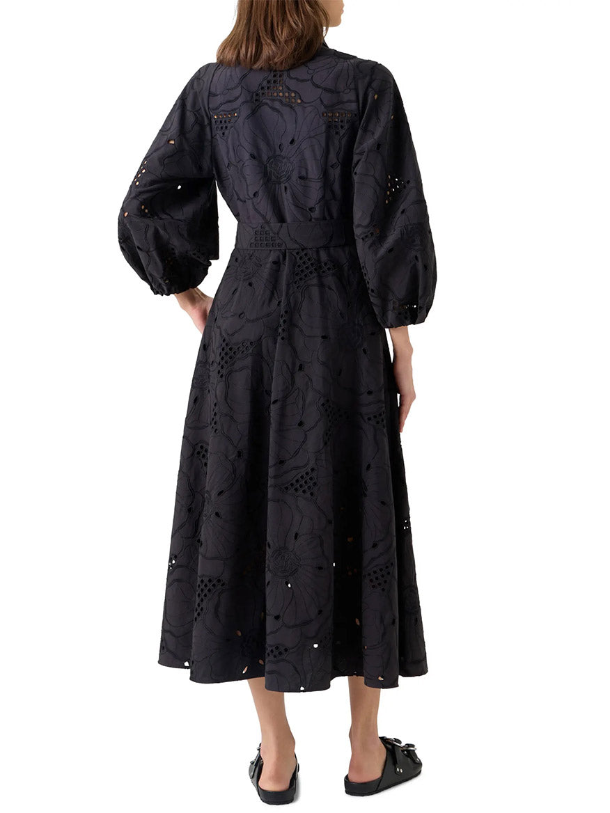 A woman is shown from the back against a white background wearing the Akris Punto Flower Eyelet Embroidered Midi Dress in Black with black slip-on shoes.