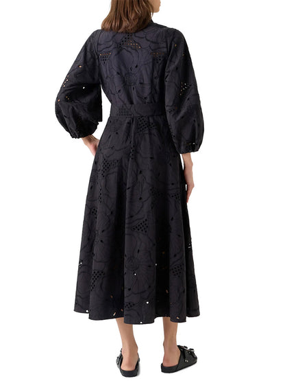 A woman is shown from the back against a white background wearing the Akris Punto Flower Eyelet Embroidered Midi Dress in Black with black slip-on shoes.