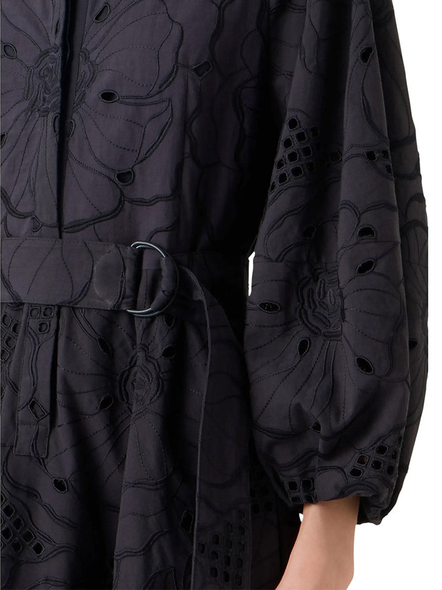Close-up of a person wearing the Akris Punto Flower Eyelet Embroidered Midi Dress in Black, featuring floral embroidery, eyelet details, and a belted waist; only the torso and part of one arm are visible.